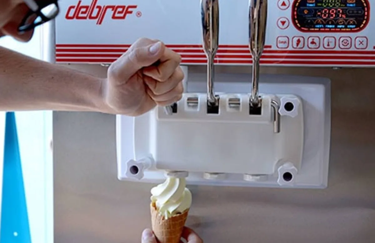 Gros plan sur le bloc de décharge d'une machine à glace italienne Debref : une main tire une manette de tirage et sert une torsade de glace dans un cornet