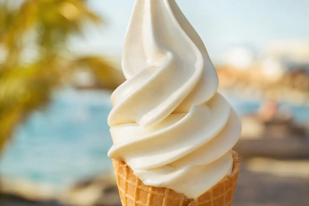 Glace italienne vanille en torsade brillante sur cornet gaufré, terrasse ensoleillée en bord de mer